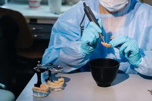 ein maskiert und behandschuhte Dental Techniker funktioniert auf ein Prothese Zahn im seine Labor foto