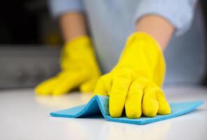 Frau im Gelb Gummi Handschuhe Tücher das Staub auf das Tabelle mit ein Lappen. Hauswirtschaft Konzept. Nahansicht. selektiv Fokus. foto