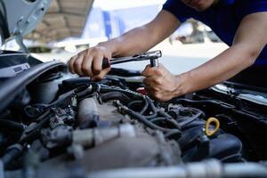 ein Mann ist Arbeiten auf ein Auto Motor. er ist mit ein Schlüssel zu lösen ein Bolzen. Konzept von Entschlossenheit und Fokus wie das Mann funktioniert zu Fix das Auto foto