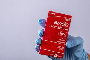 Rio, Brasilien - - Januar 27, 2023, Hand mit schützend Gummi Handschuh halten Medizin Kasten, Racecadotril foto