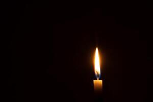 Single Verbrennung Kerze Flamme oder Licht glühend auf ein Orange Kerze auf schwarz oder dunkel Hintergrund auf Tabelle im Kirche zum Weihnachten, Beerdigung oder Denkmal Bedienung mit Kopieren Raum foto