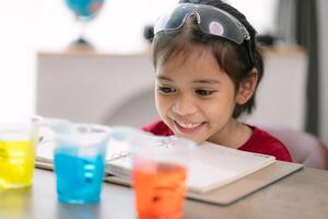 asiatisch Mädchen Herstellung Gehen Wasser Experiment. Essen Farbe ist hinzugefügt zu das Wasser im das Glas, Wasser bewegt sich entlang das Papier, und dann Farbe ist gemischt. Konzept von Wissenschaft zum Kind foto