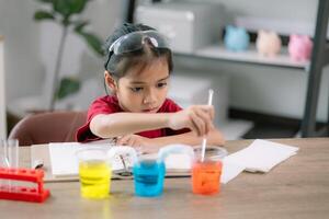 asiatisch Mädchen Herstellung Gehen Wasser Experiment. Essen Farbe ist hinzugefügt zu das Wasser im das Glas, Wasser bewegt sich entlang das Papier, und dann Farbe ist gemischt. Konzept von Wissenschaft zum Kind foto