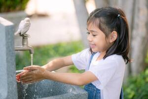 ein jung Mädchen ist Waschen ihr Hände beim ein Wasser Brunnen foto
