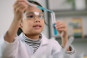 wenig süß Mädchen mit ein Mikroskop halten ein Labor Flasche mit Wasser Experiment Studie Wissenschaftler beim Schule. Bildung Wissenschaft Konzept. foto