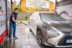 Prag, Tschechisch Republik - - April 5, 2024. jung Mann wäscht seine Auto beim ein Selbstbedienung Auto waschen mit ein Schlauch mit Druck- Wasser und Schaum. hoch Qualität Foto