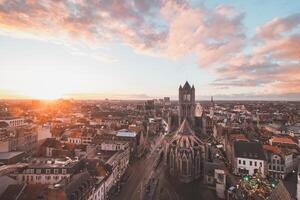 Aufpassen das Sonnenuntergang Über Gent von das historisch Turm im das Stadt Center. romantisch Farben im das Himmel. rot Licht leuchten Gent, Flandern Region, Belgien foto