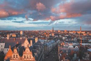 Aufpassen das Sonnenuntergang Über Gent von das historisch Turm im das Stadt Center. romantisch Farben im das Himmel. rot Licht leuchten Gent, Flandern Region, Belgien foto