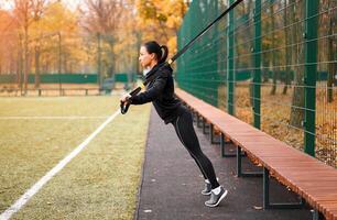 Mädchen Athlet funktional Ausbildung auf Sportplatz. gemischt Rennen jung Erwachsene Frau tun trainieren mit Suspension System. gesund Lebensstil. Dehnen draußen Spielplatz. foto