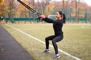 Mädchen Athlet Ausbildung mit trx auf Sportplatz. gemischt Rennen jung Erwachsene Frau tun trainieren mit Suspension System. gesund Lebensstil. Dehnen draußen Spielplatz. foto