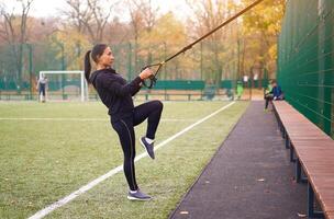 Mädchen Athlet funktional Ausbildung auf Sportplatz. gemischt Rennen jung Erwachsene Frau tun trainieren mit Suspension System. gesund Lebensstil. Dehnen draußen Spielplatz. foto