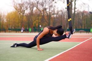 Mädchen Athlet funktional Ausbildung auf Sportplatz. gemischt Rennen jung Erwachsene Frau tun trainieren mit Suspension System. gesund Lebensstil. Dehnen draußen Spielplatz. foto