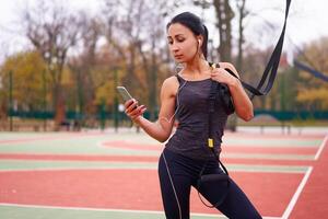 Mädchen Athlet Ausbildung mit trx auf Sportplatz. gemischt Rennen jung Erwachsene Frau tun trainieren mit Suspension System. gesund Lebensstil. Dehnen draußen Spielplatz. foto