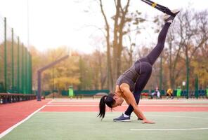 Mädchen Athlet funktional Ausbildung auf Sportplatz. gemischt Rennen jung Erwachsene Frau tun trainieren mit Suspension System. gesund Lebensstil. Dehnen draußen Spielplatz. foto