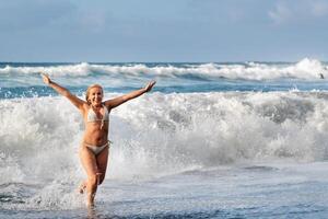 ein Mädchen mit nass Haar springt Über groß Wellen im das atlantisch Ozean, um ein Welle mit spritzt von sprühen und Wasser Tropfen.Teneriffa.Spanien foto