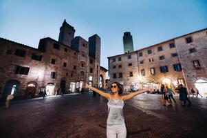 ein Mädchen im Hose und ein T-Shirt mit Brille im das Nacht Stadt von san gimignano.a Mädchen Spaziergänge um das Stadt im italien.toskana. foto