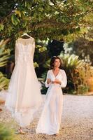 ein schön Braut steht Nächster zu ein Hochzeit Kleid mit ein Tasse von Tee im ein Boudoir Outfit Nächster zu ein Villa im italien.morgen von das Braut im Toskana foto