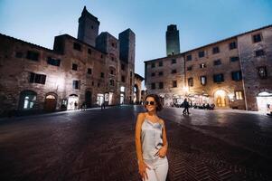 ein Mädchen im Hose und ein T-Shirt mit Brille im das Nacht Stadt von san gimignano.a Mädchen Spaziergänge um das Stadt im italien.toskana. foto