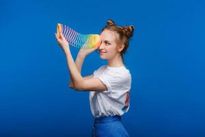 schön jung Mädchen spielen mit ein Regenbogen aufreizend, ein Spielzeug von ihr Kindheit auf ein Blau Hintergrund foto