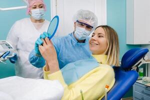 das Zahnarzt zeigt an das Klient das Ergebnisse von seine Arbeit im das Spiegel.der Klient lächelt foto