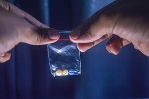 Finger halten drei Tabletten zum Schizophrene Innerhalb ein Plastik Clip auf ein dunkel Hintergrund foto