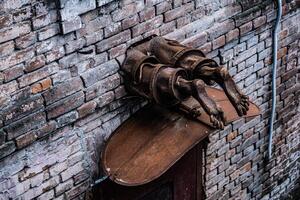 Metall Skulptur. Hälfte von niedriger Mensch Körper Stöcke aus von das Mauer. Bronze- Skulptur. modern Kunst. nackt Füße von ein Bronze- Skulptur Innerhalb das Backstein Mauer. Aussicht von über. foto