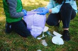 Frau Freiwillige und wenig Junge pflücken oben das Plastik Müll und Putten es im biologisch abbaubar Müllbeutel draußen. Ökologie, Recycling und Schutz von Natur Konzept. Umwelt Schutz. foto