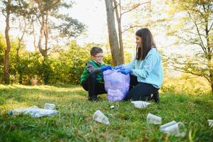 Frau Freiwillige und wenig Junge pflücken oben das Plastik Müll und Putten es im biologisch abbaubar Müllbeutel draußen. Ökologie, Recycling und Schutz von Natur Konzept. Umwelt Schutz. foto