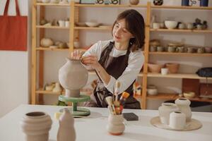 lächelnd jung weiblich Keramiker tragen Schürze Arbeit mit ungebrannt Lehm Vase im Keramik Studio foto