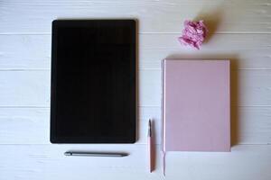ein Tablette, Notizblock, Stift und ein zerknittert Blatt von Papier auf ein Weiß hölzern Schreibtisch. foto