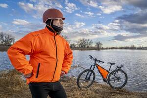 Senior männlich Radfahrer mit ein Mountin Fahrrad auf ein Ufer von See im Colorado, Winter oder früh Frühling Landschaft foto