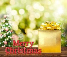 Frohe Weihnachten rotes Glitzerwort und goldenes Geschenk auf braunem Holztisch mit Weihnachtsbaum bokeh foto
