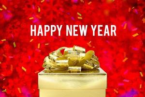 Guten Rutsch ins Neue Jahr-Wort mit goldener Geschenkbox mit Band und buntem Konfetti bei unscharfer roter Schneeflocke boekh foto