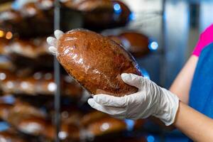 Brot im das Hände von ein Bäcker auf das Hintergrund von ein industriell Backofen und Regale mit Brot. industriell Brot Produktion. foto
