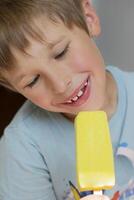 das Kind isst Eis Sahne mit Vergnügen.Junge bewundert Gelb Dessert foto