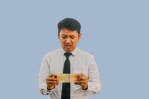 Erwachsene asiatisch Mann zeigen traurig Ausdruck während halten klein Menge von Geld foto