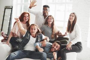 für das Bild posieren. Bürofreunde haben fröhliche Zeit beim Sitzen und Liegen auf dem weißen Sofa foto