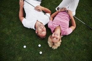 ein paar, mann und frau liegen auf dem golfplatz und entspannen nach dem spiel foto