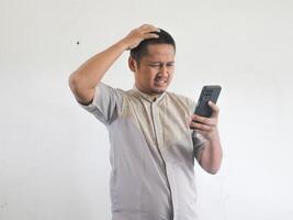 Erwachsene asiatisch Mann zeigen verwirrt Ausdruck wann suchen zu seine Telefon foto