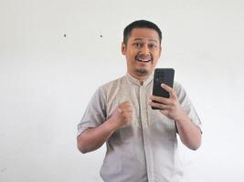 Erwachsene asiatisch Mann geballt Faust zeigen aufgeregt wann suchen zu seine Telefon foto