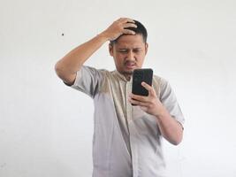 Erwachsene asiatisch Mann zeigen verwirrt Ausdruck wann suchen zu seine Telefon foto