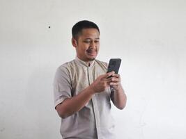 Erwachsene asiatisch Mann halten Handy, Mobiltelefon Telefon mit komisch Ausdruck foto