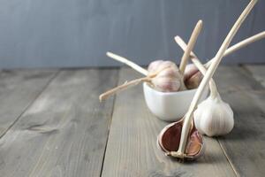 groß Köpfe von Knoblauch Lüge auf das Tabelle und im ein Schüssel auf ein grau Hintergrund mit Raum zum Copyspace Text. Rezept schblon mit Knoblauch foto