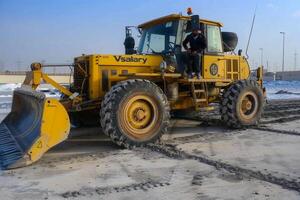 Pistenfahrzeug im das Mitte Ost. Grader geparkt auf Beton Platten beim ein industriell Komplex foto