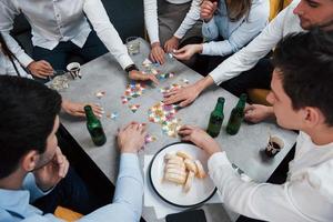 Ansicht von oben. Entspannung mit Spiel. erfolgreiches Geschäft feiern. Junge Büroangestellte sitzen mit Alkohol am Tisch foto