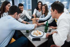 Essen, Tasse und Flaschen. erfolgreiches Geschäft feiern. Junge Büroangestellte sitzen mit Alkohol am Tisch foto
