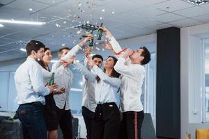 für unsere Zukunft. Foto eines jungen Teams in klassischer Kleidung, das den Erfolg feiert, während es im modernen, gut beleuchteten Büro Getränke hält