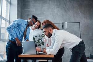 Tisch umgeben. vier junge geschäftsleute, die an dem plan arbeiten, verwenden notebook foto