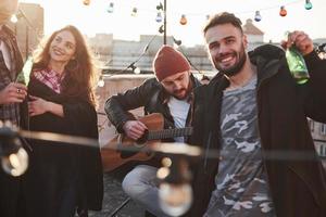 Zeit entspannen. schöne junge freunde. Dachparty mit Alkohol und Akustikgitarre am sonnigen Herbsttag foto