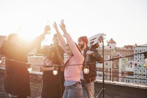 Hände hoch. junge Leute verbringen sonnigen Herbsttag auf dem Dach mit Gitarre und Getränken foto